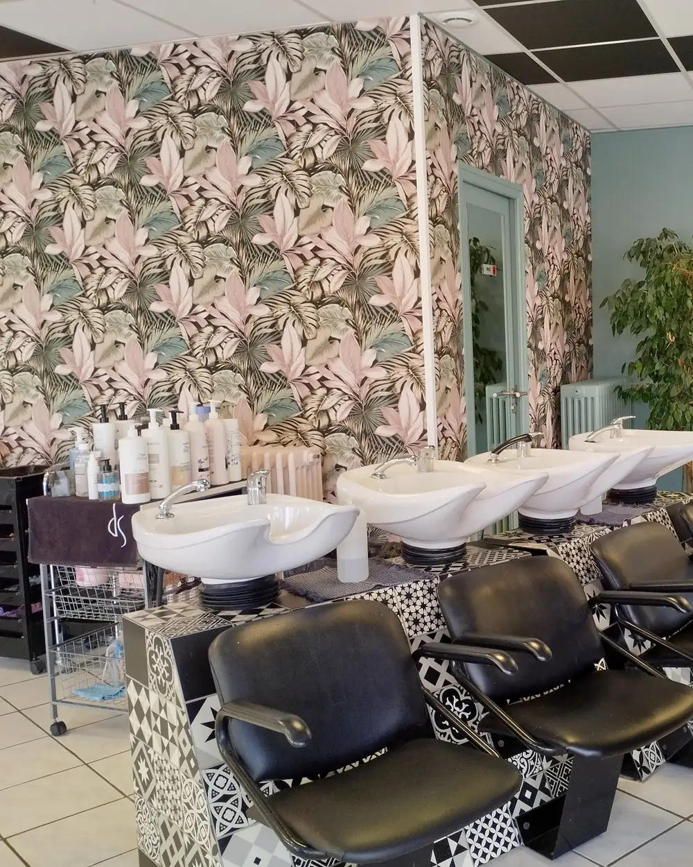 Les bacs à shampooing du salon devant le papier peint à grandes feuilles roses et vertes